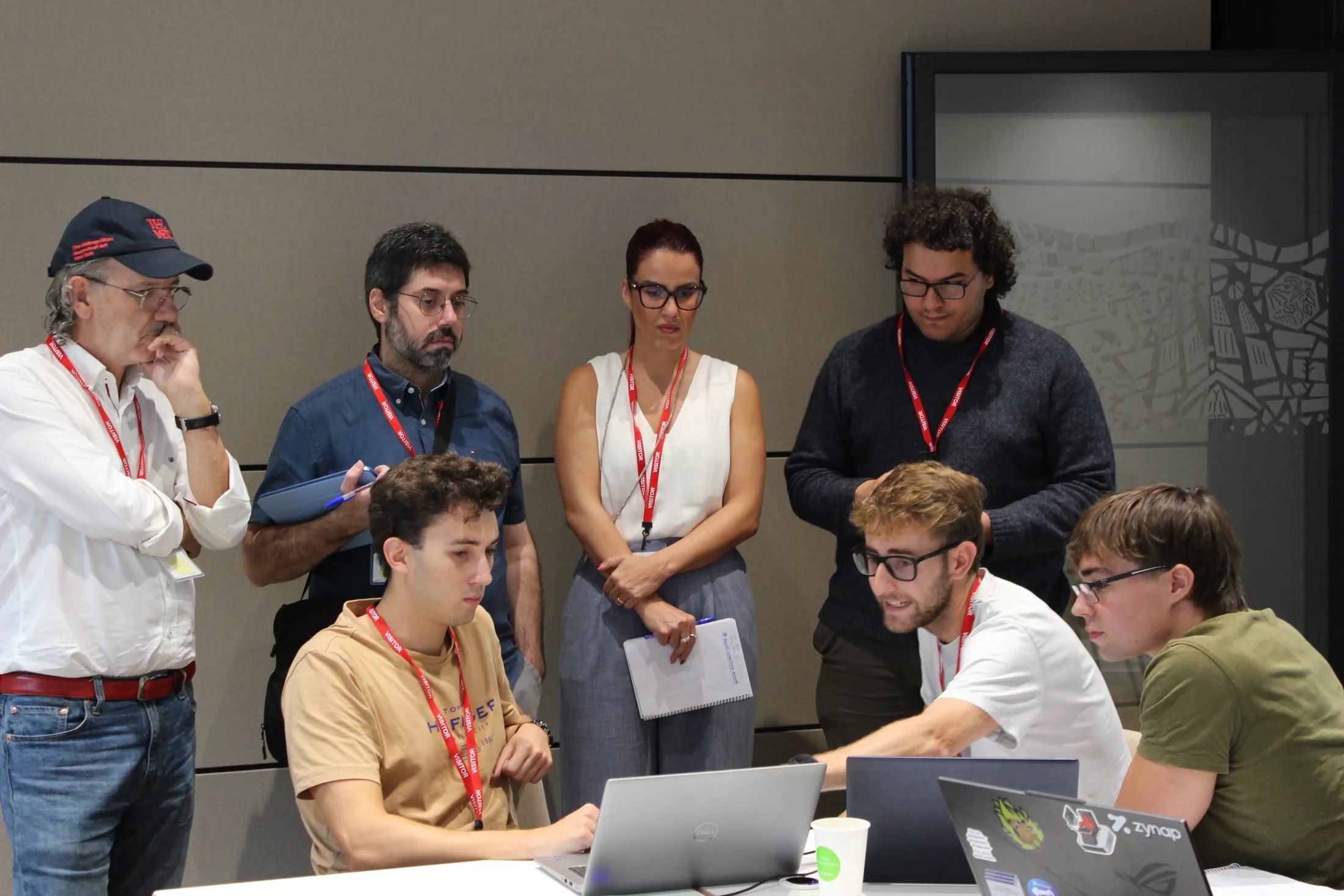 Team members working on a laptop while mentors look on and discuss